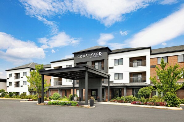 A Courtyard by Marriott hotel with a covered entrance, brick and white exterior, and landscaped gardens. - Courtyard by Marriott Concord (Concord)