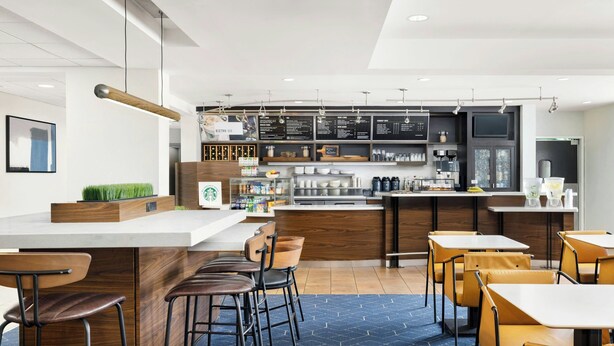 A modern cafe with wooden bar counters, bar stools, and tables. There are menu boards above the bar area. - Courtyard by Marriott Concord (Concord)