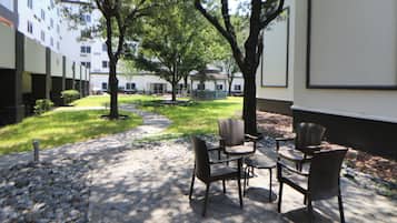 An outdoor patio area with stone flooring, a seating arrangement of chairs and tables, and a pathway leading to a building.
