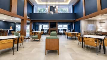 A spacious hotel lobby with multiple seating areas, a central fireplace, and large windows providing natural light.