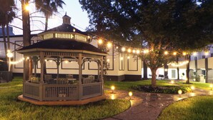 Um gazebo com assentos, cercado por um gramado bem cuidado e um caminho pavimentado.