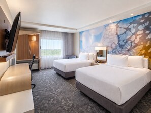 A hotel room with two beds, a desk, a chair, a television, and a large window with curtains. - Courtyard by Marriott Monterrey Airport (Apodaca)