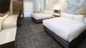 Quarto de hotel com duas camas, uma escrivaninha, uma televisão e uma janela grande com cortinas.
