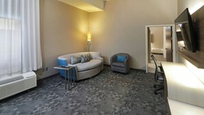 Quarto de hotel com sofá, poltrona, escrivaninha, televisão e abajur.