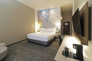 A hotel room with a bed, bedside tables, a desk with a coffee maker, a TV, and a wall with a decorative mural. - Courtyard by Marriott Monterrey Airport (Apodaca)