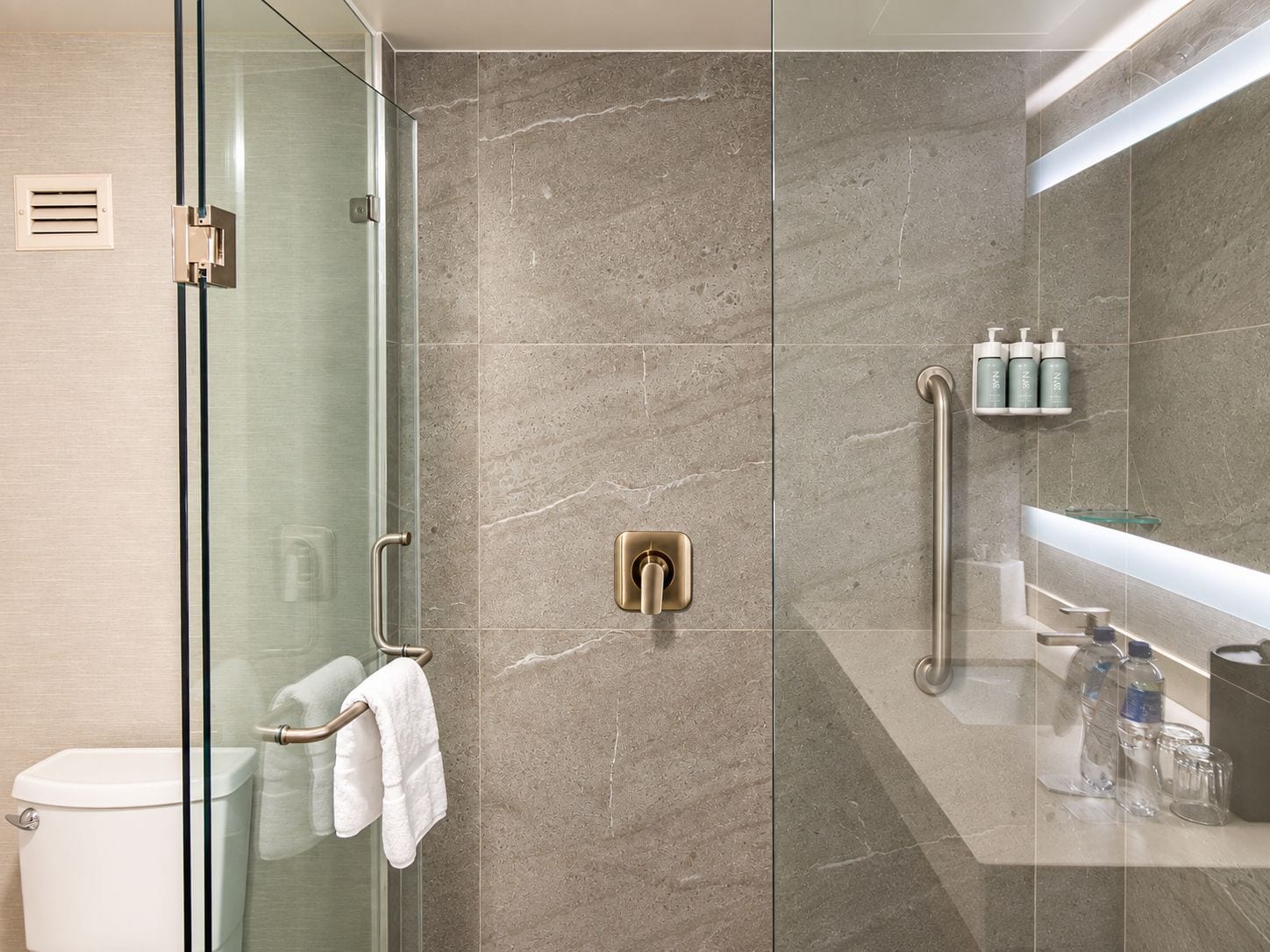 A modern bathroom with a glass shower enclosure, a toilet, and a vanity with toiletries.