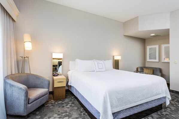 A hotel room with a large bed, a chair, a desk, and a lamp.