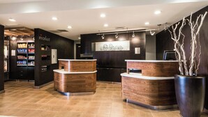 A reception area with wooden reception desks, a wall-mounted artwork, and a large potted plant. - Courtyard by Marriott Rocky Mount (Rocky Mount)