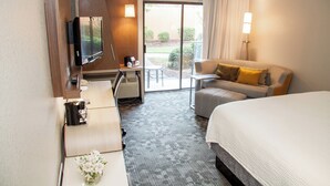 A hotel room with a bed, a desk with a computer, a TV, a sofa, and a view of the outdoors. - Courtyard by Marriott Rocky Mount (Rocky Mount)