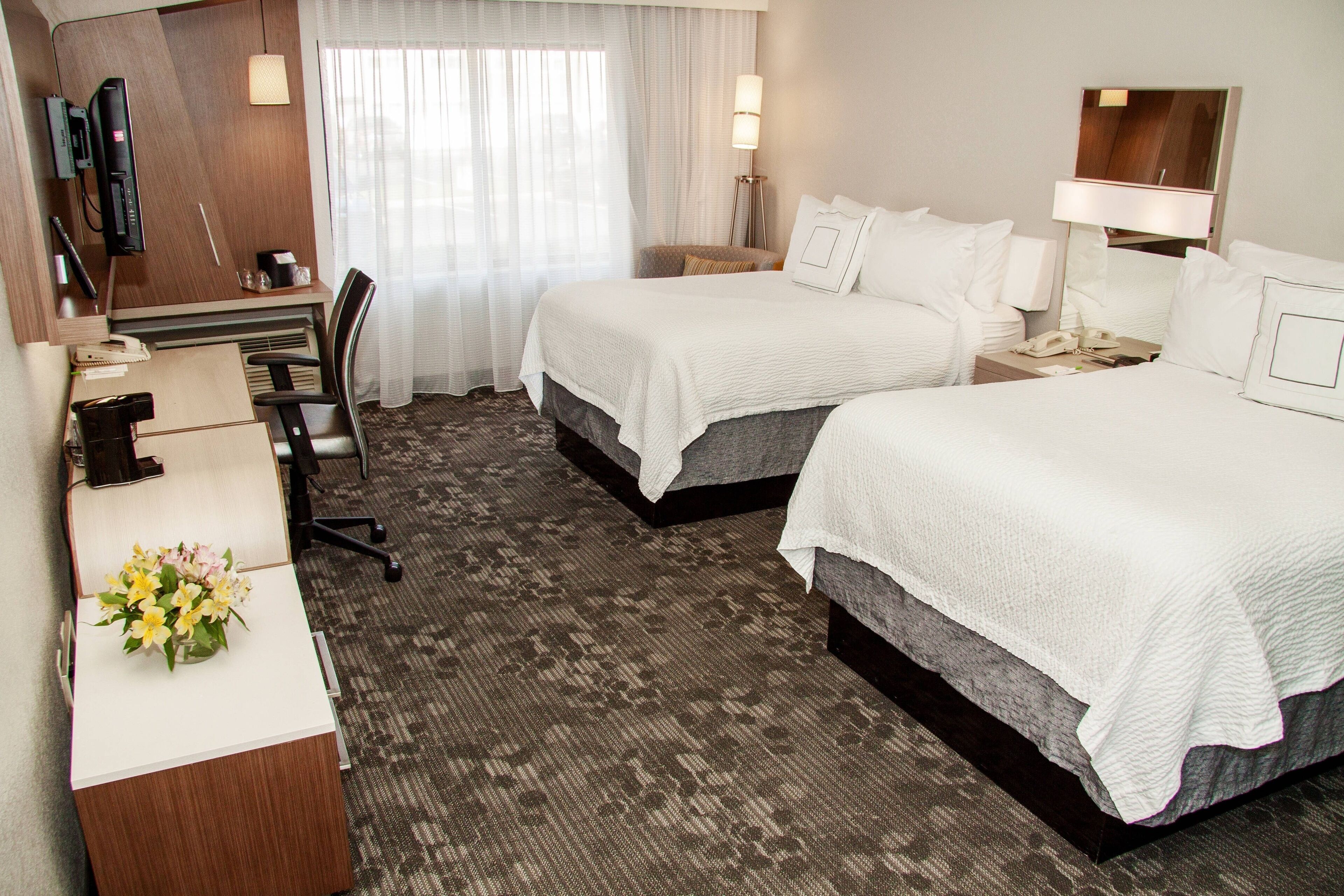 A hotel room with two beds, a desk with a telephone, and a chair.