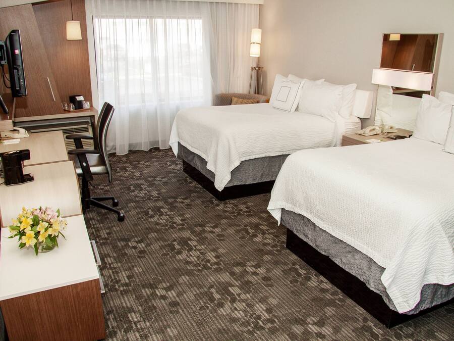 A hotel room with two beds, a desk with a telephone, and a chair.