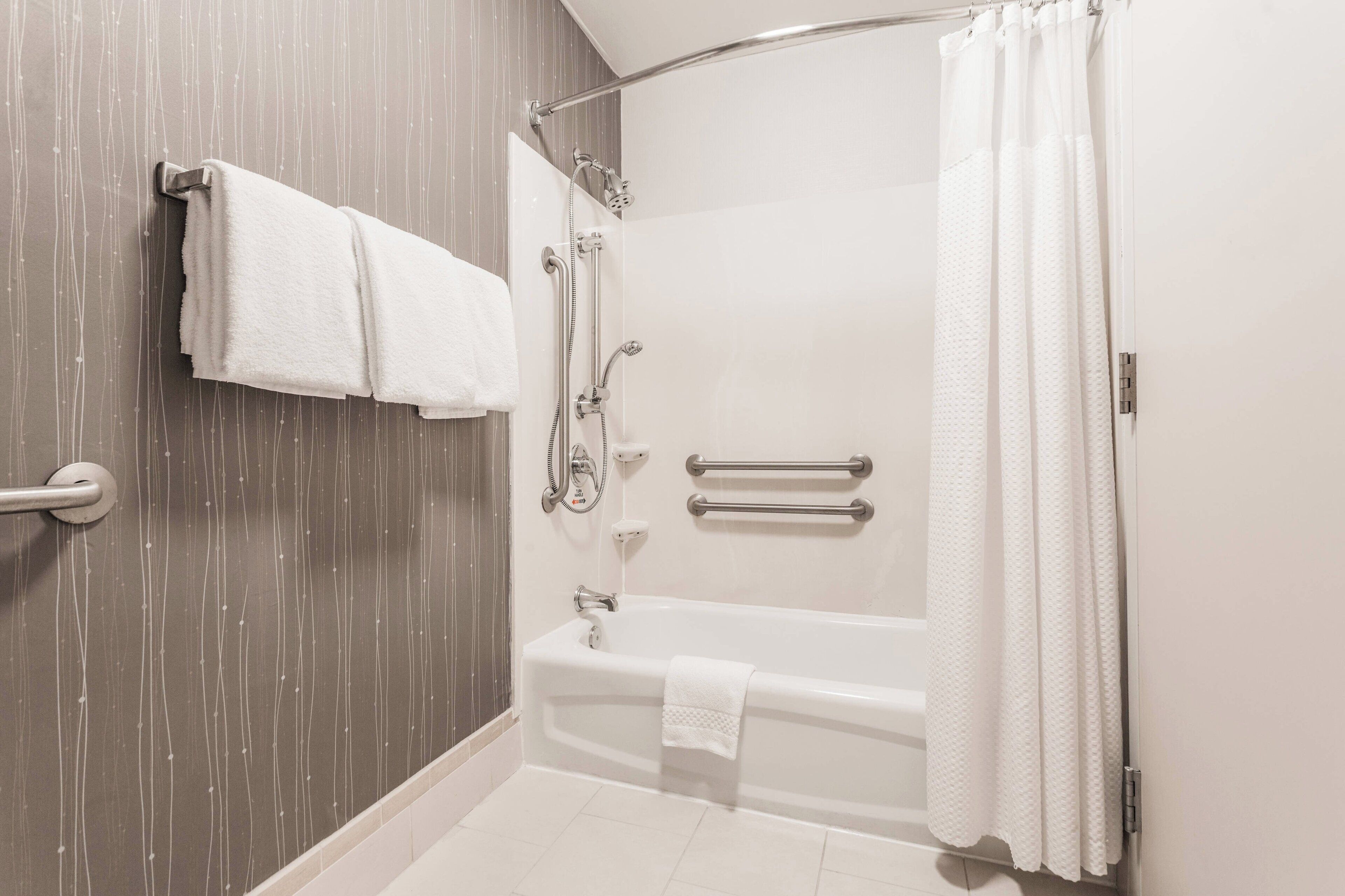 Un baño moderno con bañera, ducha y barras de apoyo.