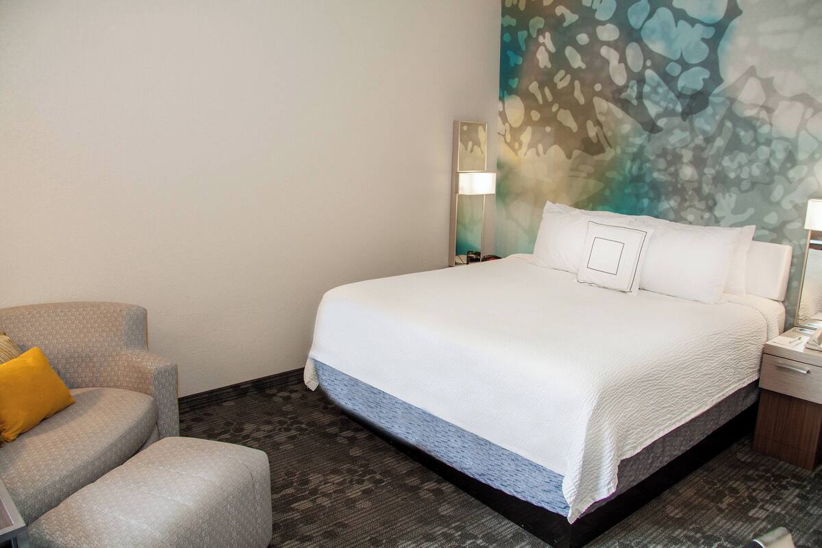 Une chambre d’hôtel avec un grand lit, une chaise, une table de chevet et un mur orné d’une fresque à motifs.