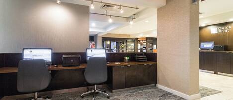 Un'area reception di un hotel con due postazioni computer, un angolo salotto e un angolo ristoro Starbucks.