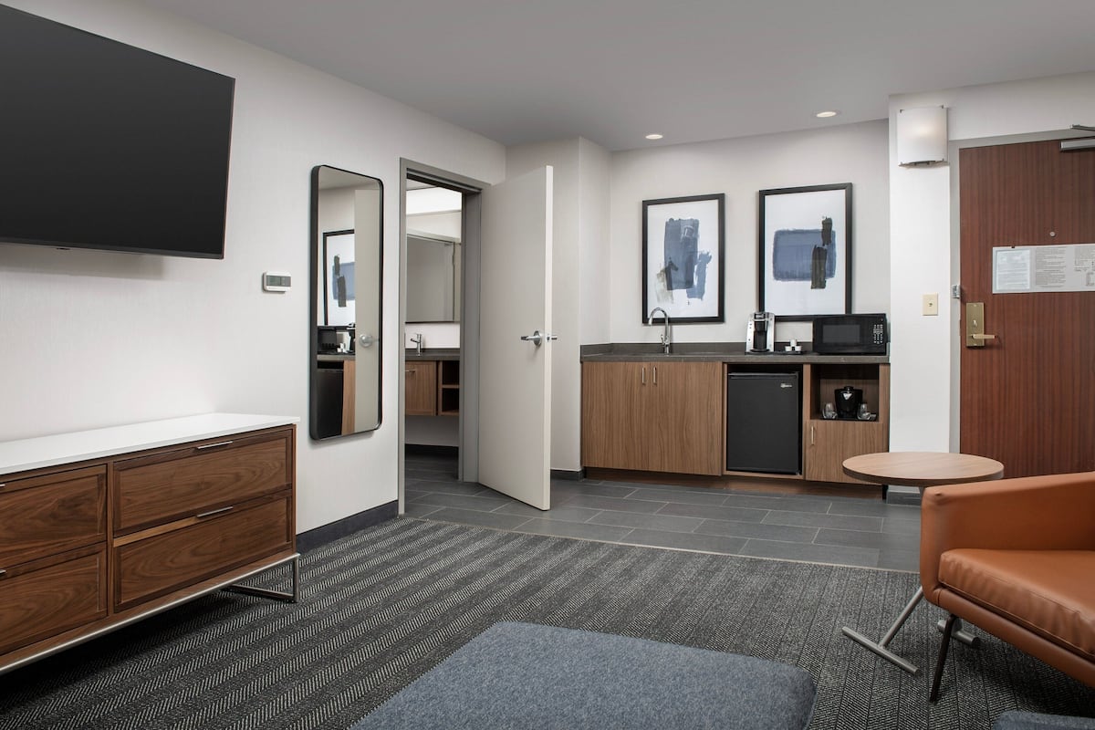 Een moderne hotelkamer met een flatscreen televisie, een houten dressoir, een ronde salontafel en een zithoek.