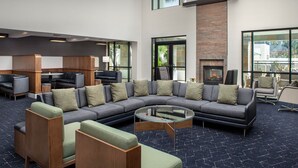 A modern lounge area with a sectional sofa, armchairs, a glass coffee table, and a fireplace.
