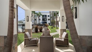 A covered outdoor seating area with wicker furniture, a view of a pool, and a building in the background.