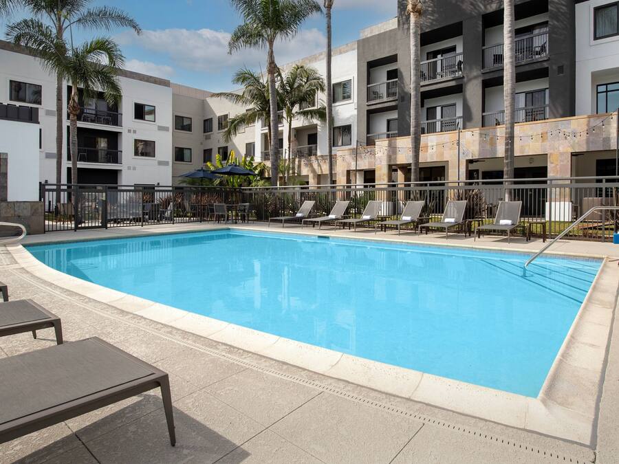 Piscina com espreguiçadeiras e palmeiras, rodeada por um edifício com varandas.
