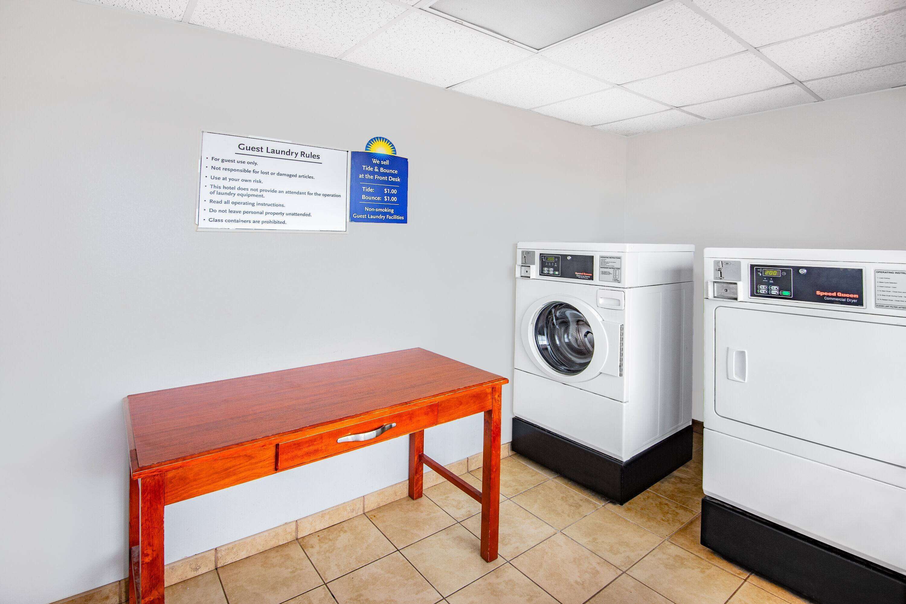 A laundry room with a wooden table, two washing machines, and a sign detailing guest laundry rules.