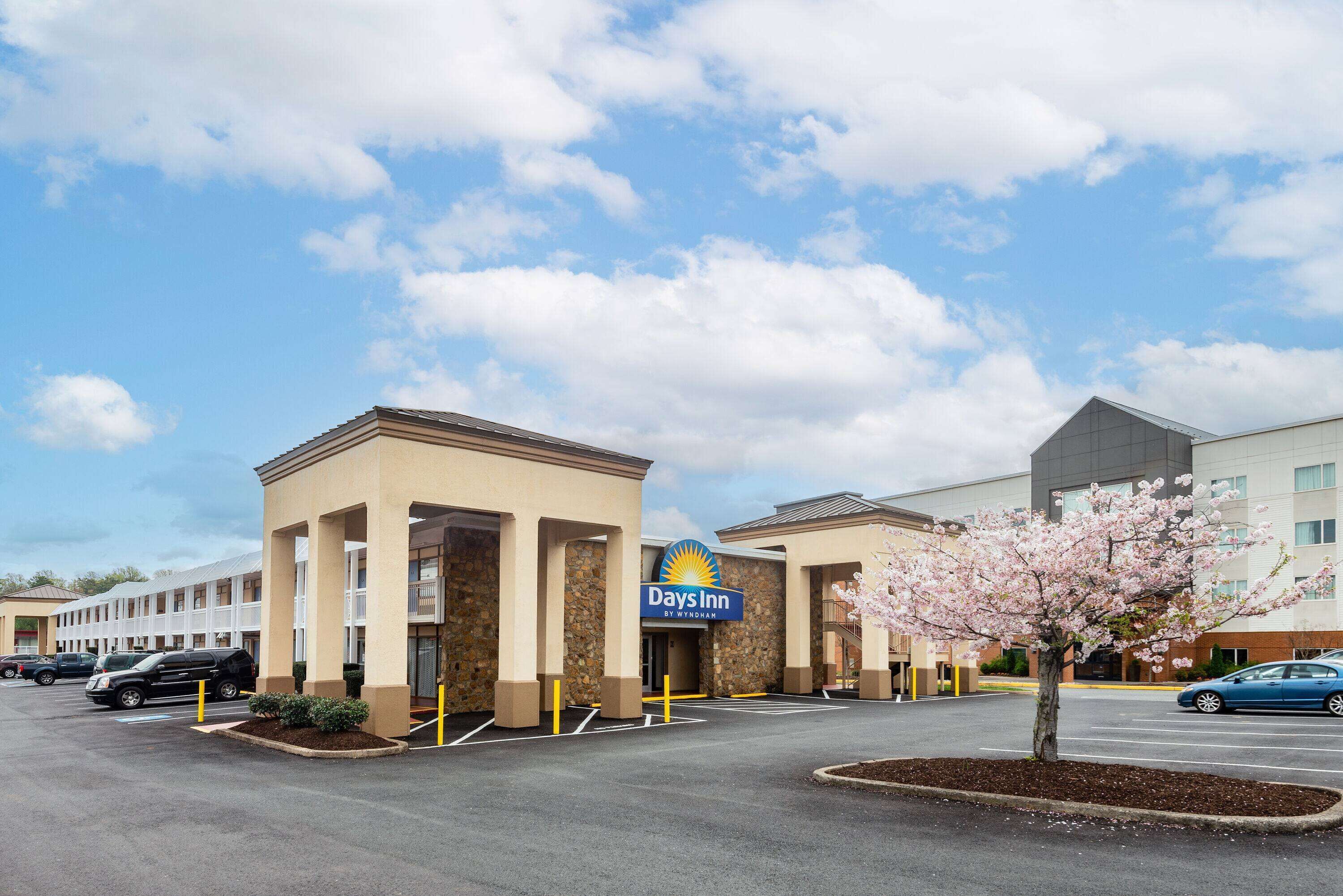 A Days Inn building with a stone facade, a parking lot, and a cherry blossom tree in front.