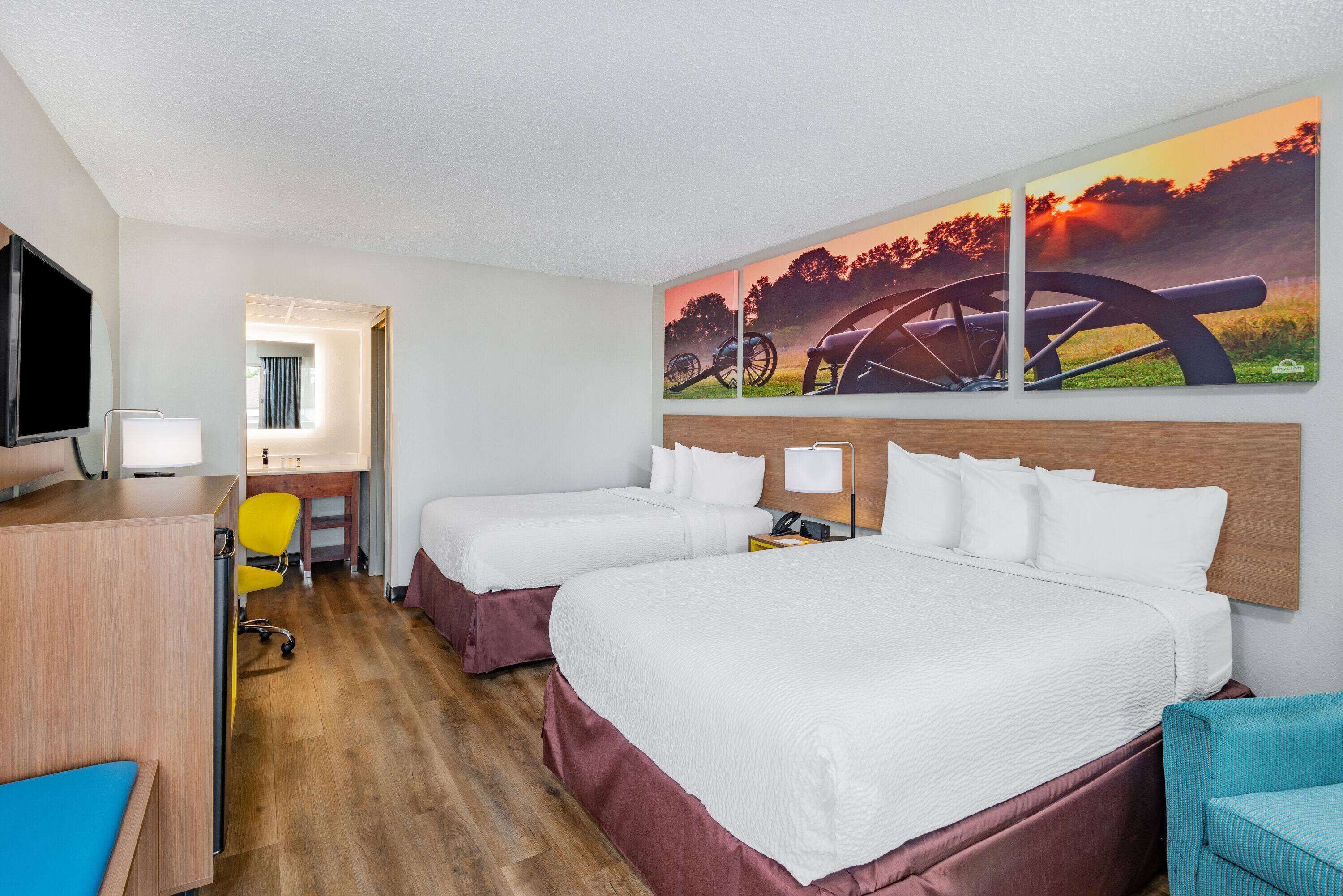 Habitación de hotel con dos camas, un escritorio, una silla y un televisor.