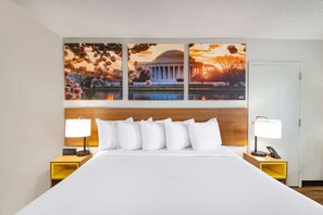 A hotel room with a large bed, two bedside tables, and a wall-mounted artwork depicting a sunset over a classical building. - Days Inn by Wyndham Charlottesville/University Area (Charlottesville)