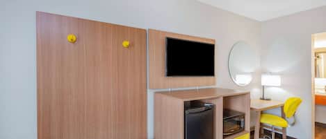 Kompakti hotellihuone, jossa on puinen vaatekaappi, taulutelevisio, pieni jääkaappi, työpöytä tuolilla ja peili.