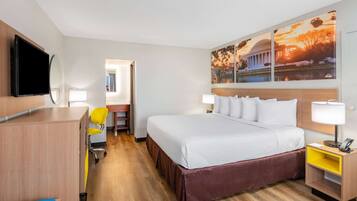 Habitación de hotel con cama, escritorio, silla, televisión y obras de arte en la pared.