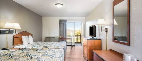 A hotel room with a large bed, a desk, a TV, and a balcony with a view.