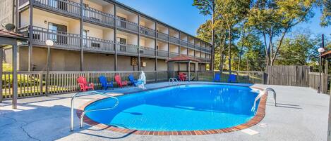A swimming pool with a brick border, surrounded by a wooden deck and a fence.