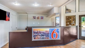A reception area with a brown counter, a large number '6' sign, and a 'We'll leave the light on for you' sign. - Motel 6 Hot Springs, AR (Hot Springs)