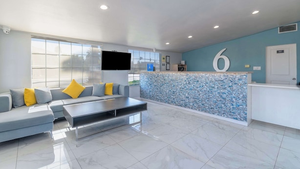A modern hotel lobby with a reception desk, a large sofa with cushions, a flat-screen TV, and a tiled floor. - Studio 6 Suites Madera, California - Yosemite (Madera)