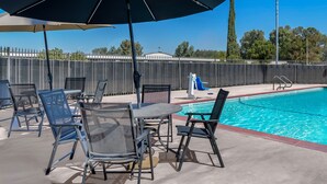 A poolside area with outdoor seating and a large umbrella. - Studio 6 Suites Madera, California - Yosemite (Madera)
