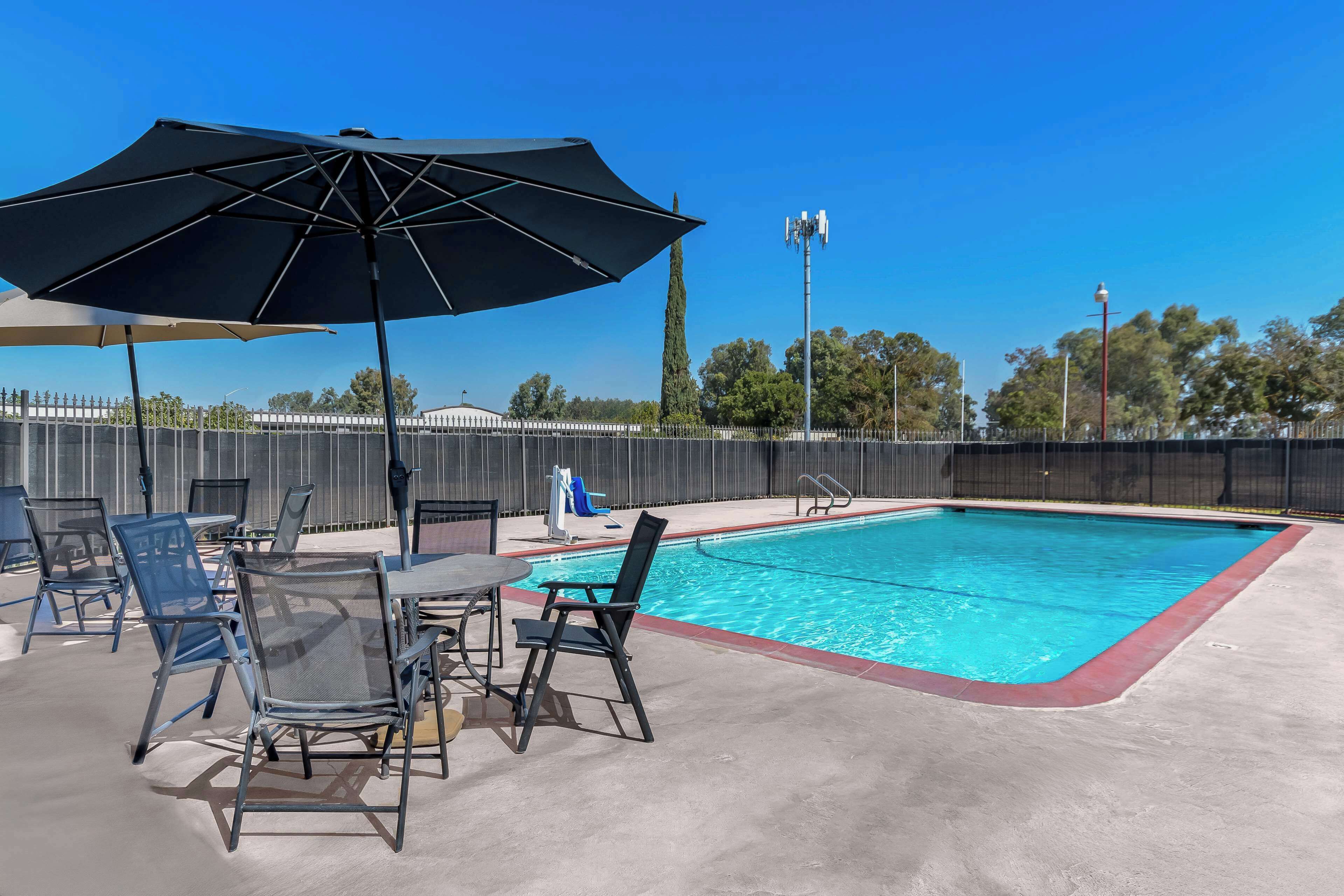 A pool area with a table and chairs, a large umbrella, and a fenced pool.
