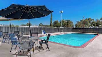 A pool area with a table and chairs, a large umbrella, and a fenced pool.