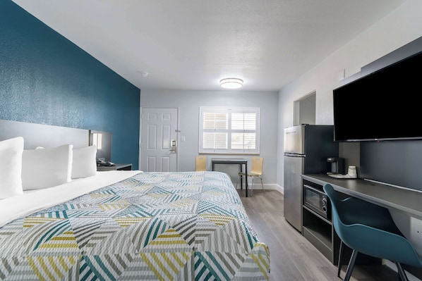 A hotel room with a bed, a desk, a chair, a television, and a refrigerator. - Studio 6 Suites Madera, California - Yosemite (Madera)
