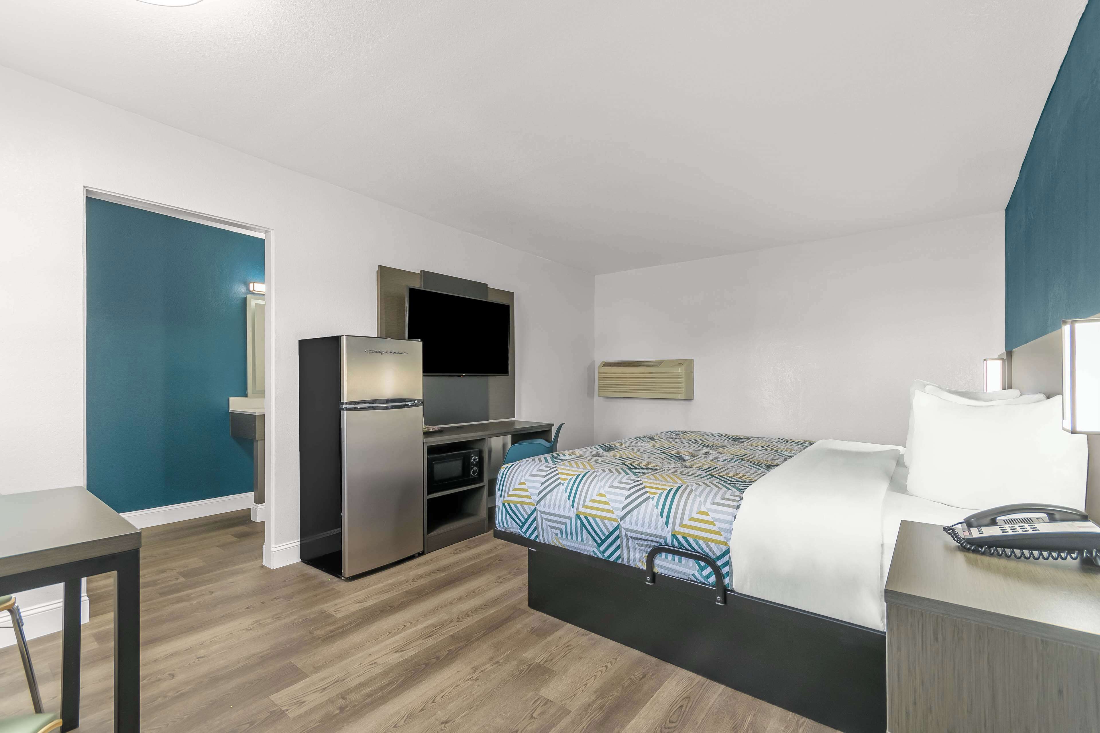 A compact hotel room with a bed, a desk, a refrigerator, and a television.