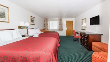 A hotel room with two beds, a desk, a chair, a TV, and a door.
