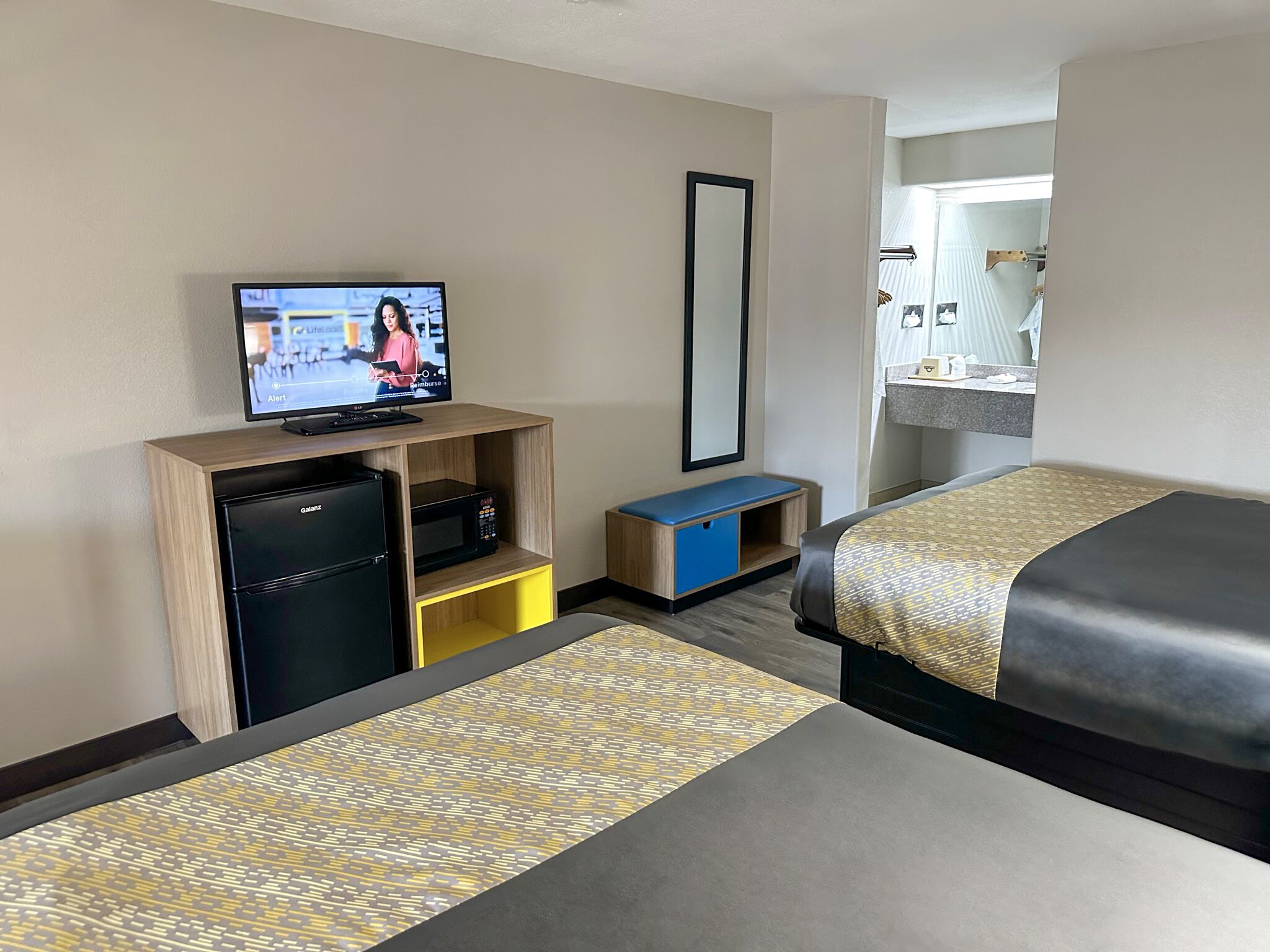 Une chambre d’hôtel équipée d’une télévision, d’un bureau avec un ordinateur, d’un miroir et de deux lits.