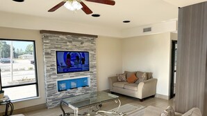 A modern living room with a stone accent wall, a flat-screen TV, a glass coffee table, and a beige sofa. - Days Inn & Suites by Wyndham Opelousas (Opelousas)