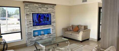 A modern living room with a stone accent wall, a flat-screen TV, a glass coffee table, and a beige sofa.