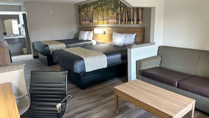 A hotel room with two beds, a sofa, a chair, and a wooden table. - Days Inn & Suites by Wyndham Opelousas (Opelousas)