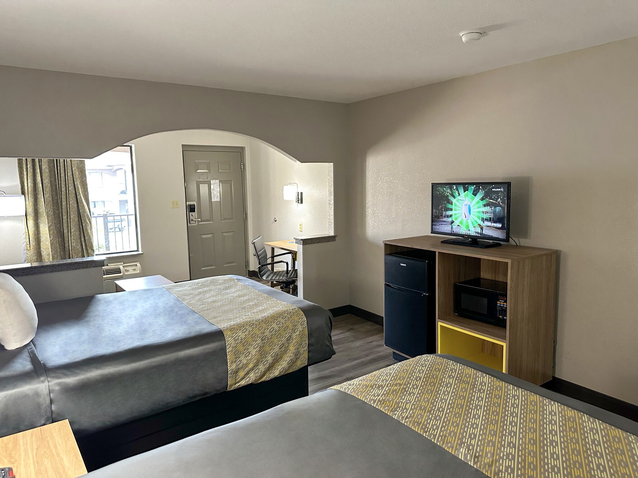 A hotel room with two beds, a desk, a television, and a minibar.