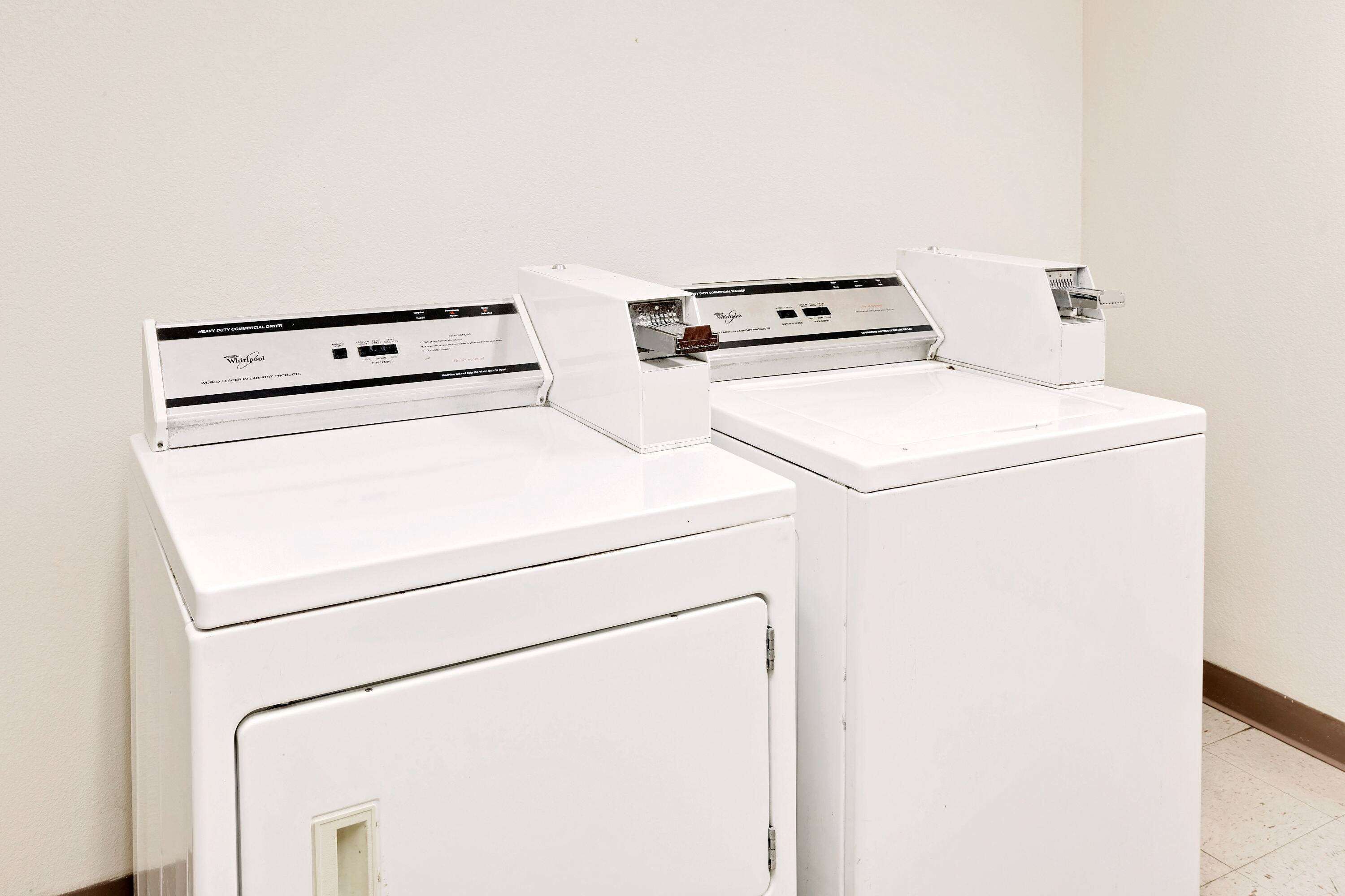 Two white front-loading washing machines in a room with a plain white wall and a tiled floor.