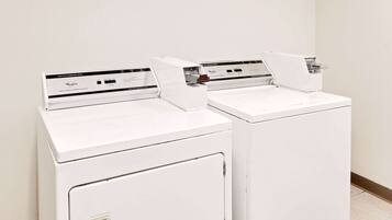 Two white front-loading washing machines in a room with a plain white wall and a tiled floor.