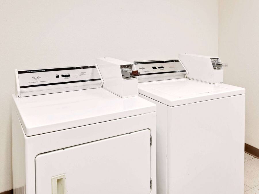 Two white front-loading washing machines in a room with a plain white wall and a tiled floor.