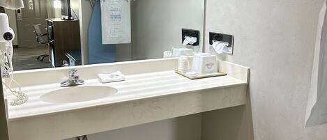 A hotel bathroom with a large mirror, a sink, and a shower area.