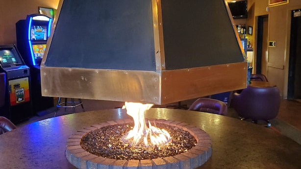 A fire feature with a metal structure and a brick base, surrounded by a concrete floor.