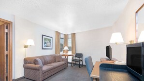 A hotel room with a sofa, a chair, a TV, and a desk with a lamp.
