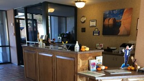 A reception area with a wooden counter, a Days Inn logo on the floor mat, a clock, and a framed picture of a rock formation.